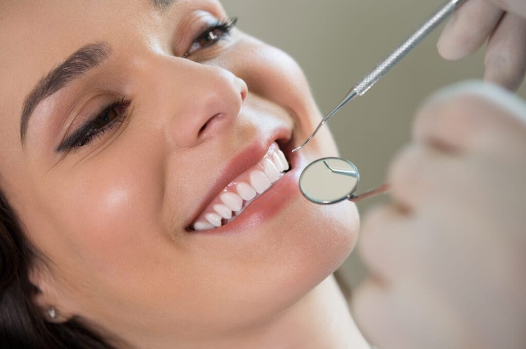 Closeup of a dentist examining a young woman’s teeth with a mirror and dental instrument