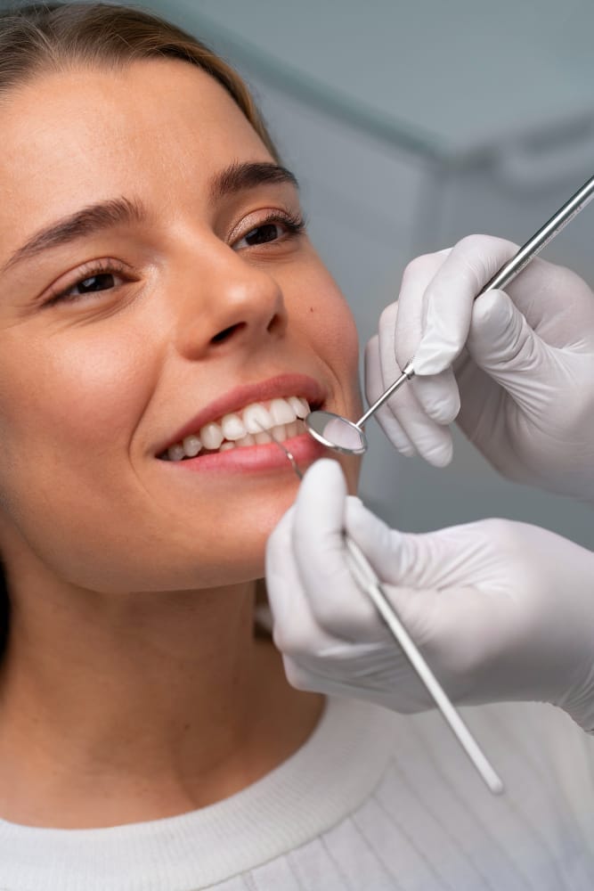 A close-up of a woman smiling while a dentist examines her teeth using dental tools.