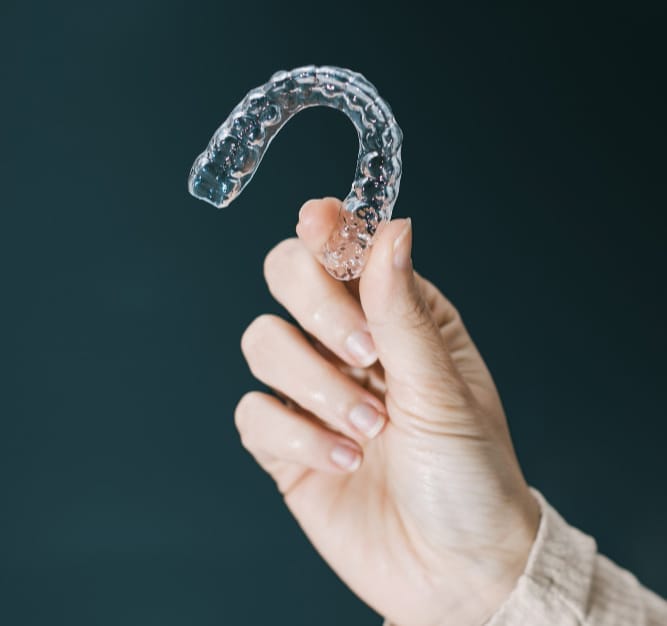 A hand holding a clear dental aligner against a dark background.