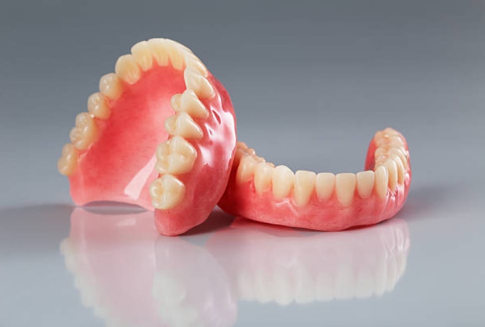 A set of upper and lower full dentures displayed on a reflective surface.