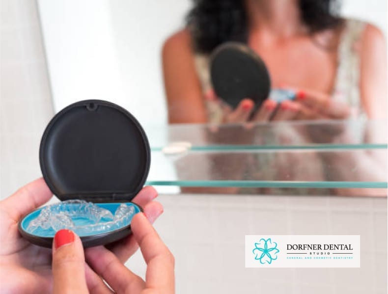 A person holding a dental aligner case in front of a mirror, with the Dorfner Dental Studio logo in the corner.