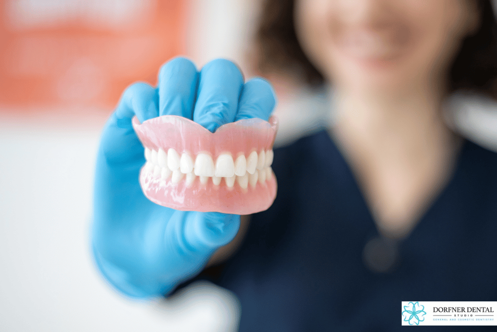 Dental professional at Dorfner Dental Studio holding a full denture model to explain denture lifespan